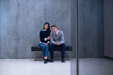 Image showing business couple using mobile phone while sitting on the bench