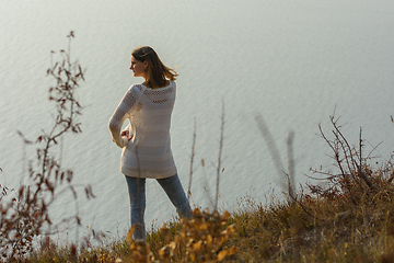 Image showing A girl stands on a hill by the sea and looks around, rear view