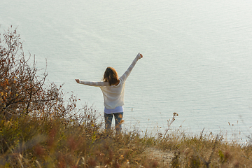 Image showing Happy girl happily raised her hands up enjoying the seascape, view from the back