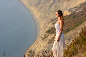 Image showing Beautiful slender girl in a white dress on the background of a beautiful mountain and sea landscape