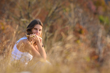 Image showing A girl sits in a field, against a background of blurred wildflowers and looks into the frame