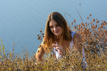Image showing A girl collects wildflowers on a slope by the sea