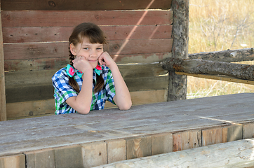 Image showing Portrait of a beautiful girl of ten years old sitting at a wooden table in nature