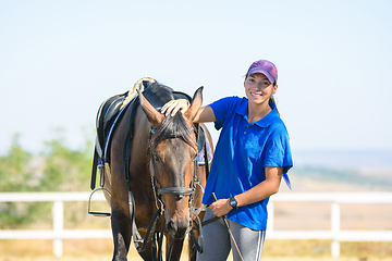 Image showing Portrait of a beautiful girl in casual clothes standing next to a horse and joyfully looking into the frame