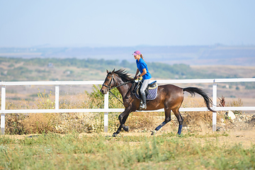 Image showing Girl rides a horse along the fence of the corral