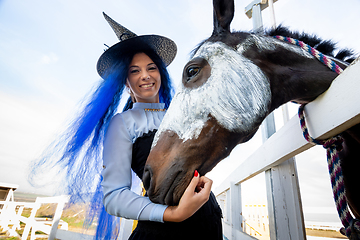 Image showing A girl dressed as a witch stands next to a horse on which a skeleton is drawn for the celebration of Halloween