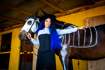 Image showing Halloween celebration, a young girl in a witch costume stands by a horse with a skeleton drawn