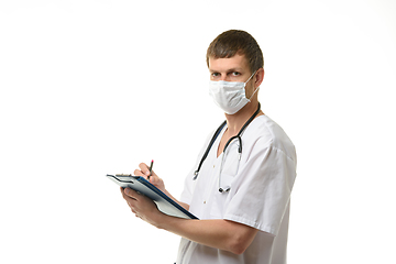 Image showing A male doctor writes in a clipboard with a ballpoint pen and looked into the frame