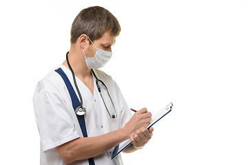 Image showing Male doctor writes with his right hand in a clipboard with a ballpoint pen