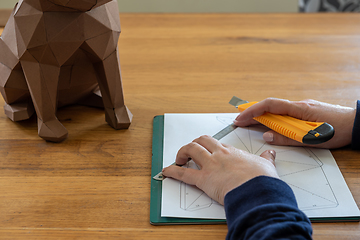 Image showing Somebody is making a cube sculpture with paper, linear and knife