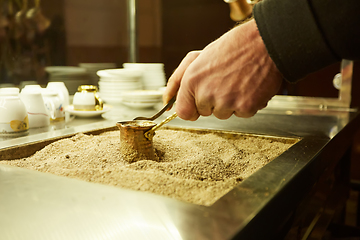 Image showing Close up hands of a man cooking turkish coffee on hot golden sand.