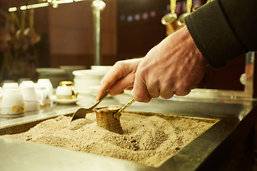 Image showing Close up hands of a man cooking turkish coffee on hot golden sand.