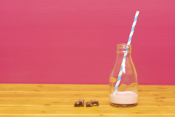 Image showing Straw and half bottle of strawberry milkshake with cookie crumbs