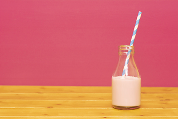 Image showing Milk bottle half full with strawberry milkshake with a straw