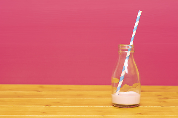 Image showing Milk bottle with dregs of strawberry milkshake and a straw