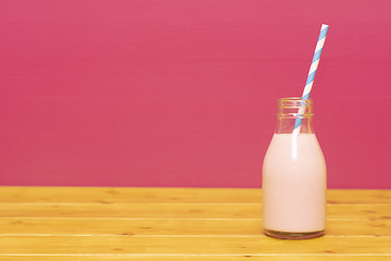 Image showing Strawberry milkshake with a straw in a glass milk bottle