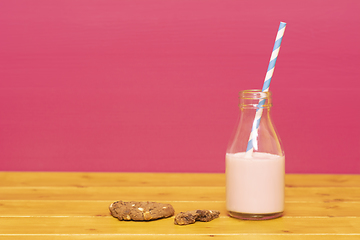 Image showing Half bottle of strawberry milkshake with straw and half-eaten co