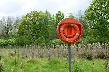 Image showing Bright orange life belt on a pole near a deep pond filled with b