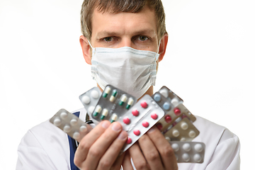 Image showing A man in a medical mask holds a fan of medicines in front of him