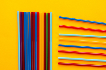 Image showing On a yellow background, multicolored cocktail tubes lie, next to a bunch of vertical tubes lie horizontal