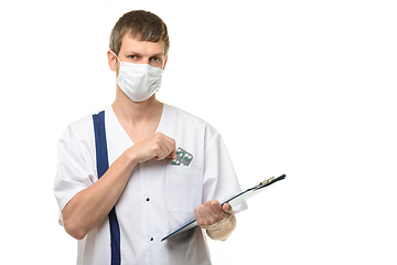 Image showing The doctor stands with a tablet in his hand, with the other hand he pulls out medicines from the chest pocket