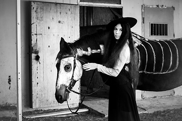 Image showing Black and white portrait of a girl in a witch costume with a horse on which a skeleton is drawn