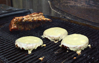 Image showing Three cheeseburgers and a rack of lamb on a grill