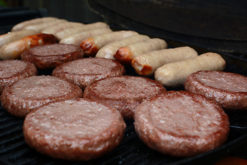 Image showing Burgers and sausages starting to cook on a grill