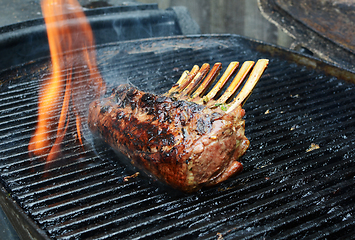 Image showing Flame rises from a grill around barbecued meat