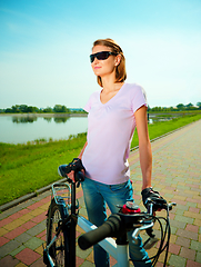 Image showing Young woman is standing behind bicycle