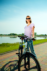 Image showing Young woman is standing behind bicycle