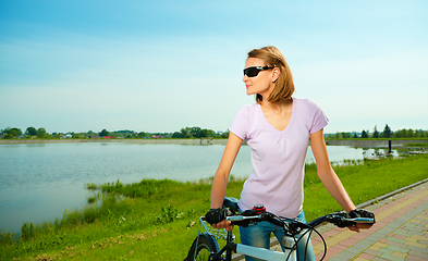 Image showing Young woman is standing behind bicycle