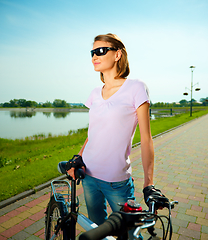 Image showing Young woman is standing behind bicycle