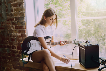 Image showing Woman recording music, playing guitar and singing at home