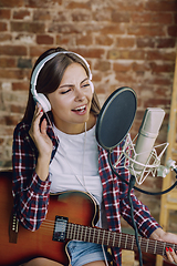 Image showing Woman recording music, playing guitar and singing at home