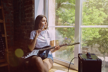 Image showing Woman recording music, playing guitar and singing at home