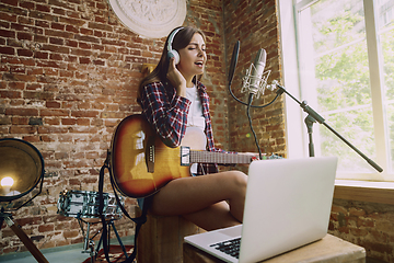 Image showing Woman recording music, playing guitar and singing at home