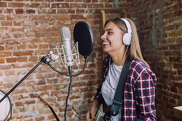 Image showing Woman recording music, playing guitar and singing at home