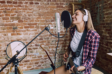 Image showing Woman recording music, playing guitar and singing at home