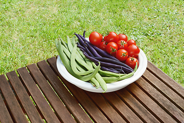 Image showing Freshly harvested beans and cherry tomatoes on a wooden table 