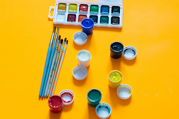 Image showing Brushes, jars of gouache and watercolor paints lie on a yellow background