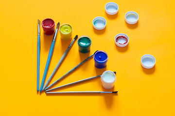 Image showing On a yellow background, brushes and jars of gouache are laid out, lids are randomly laid out