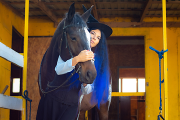 Image showing A girl dressed as a witch hugs a horse and looks thoughtfully into the distance