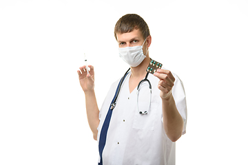 Image showing A male doctor holds a syringe with a medicine in one hand and a pill in the other hand