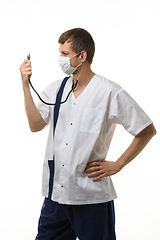 Image showing Doctor in a mask looks at a phonendoscope dressed on himself