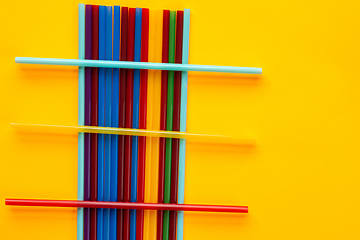 Image showing On a yellow background are multi-colored cocktail tubes, on a heap of vertical tubes are three horizontal