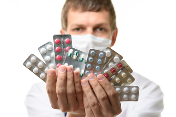 Image showing A man in a medical mask sips a fan of medicines into the frame, focusing on medicines