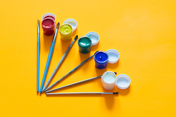 Image showing Brushes and jars of gouache are laid out on a yellow background