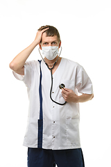 Image showing Doctor in a mask listens to his heart, with the other hand holds his sore head, isolated on white background