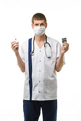 Image showing Portrait of a doctor holding a syringe with medicine in one hand and pills in the other hand, isolated on white background